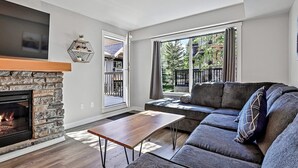 A living room with a stone fireplace, a large flat-screen TV, a grey sofa, and a wooden coffee table.