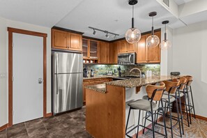 Una cocina con armarios de madera, electrodomésticos de acero inoxidable y una zona de bar con taburetes.