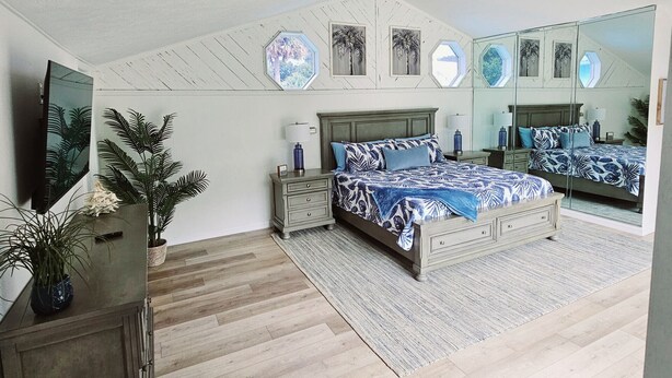 Ein Schlafzimmer mit einem Bett, einem Nachttisch, einer Kommode, einem Deckenventilator und einem großen Spiegel.