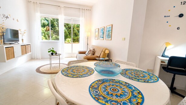 A modern living room with a round dining table, a sofa, a TV, and a window with curtains. - Appartamenti Abate Perla del Golfo Home (Alcamo)