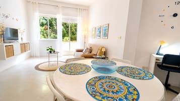 Un salon moderne avec une table à manger ronde, un canapé, un téléviseur et une fenêtre avec des rideaux.