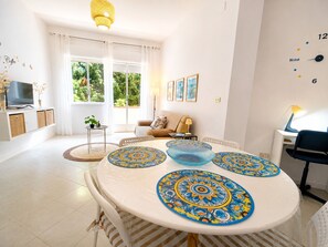 Un salon moderne avec une table à manger ronde, un canapé, un téléviseur et une fenêtre avec des rideaux.