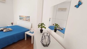 A bedroom with two beds, a small white table, a potted plant, a decorative mirror, and a wall-mounted air conditioner. - Appartamenti Abate Perla del Golfo Home (Alcamo)