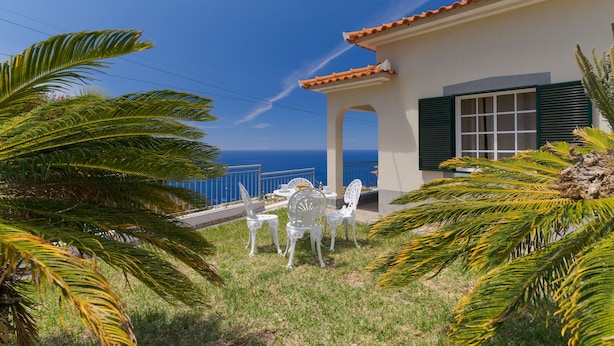 Een terras met witte stoelen en een tafel, met uitzicht op de kust.