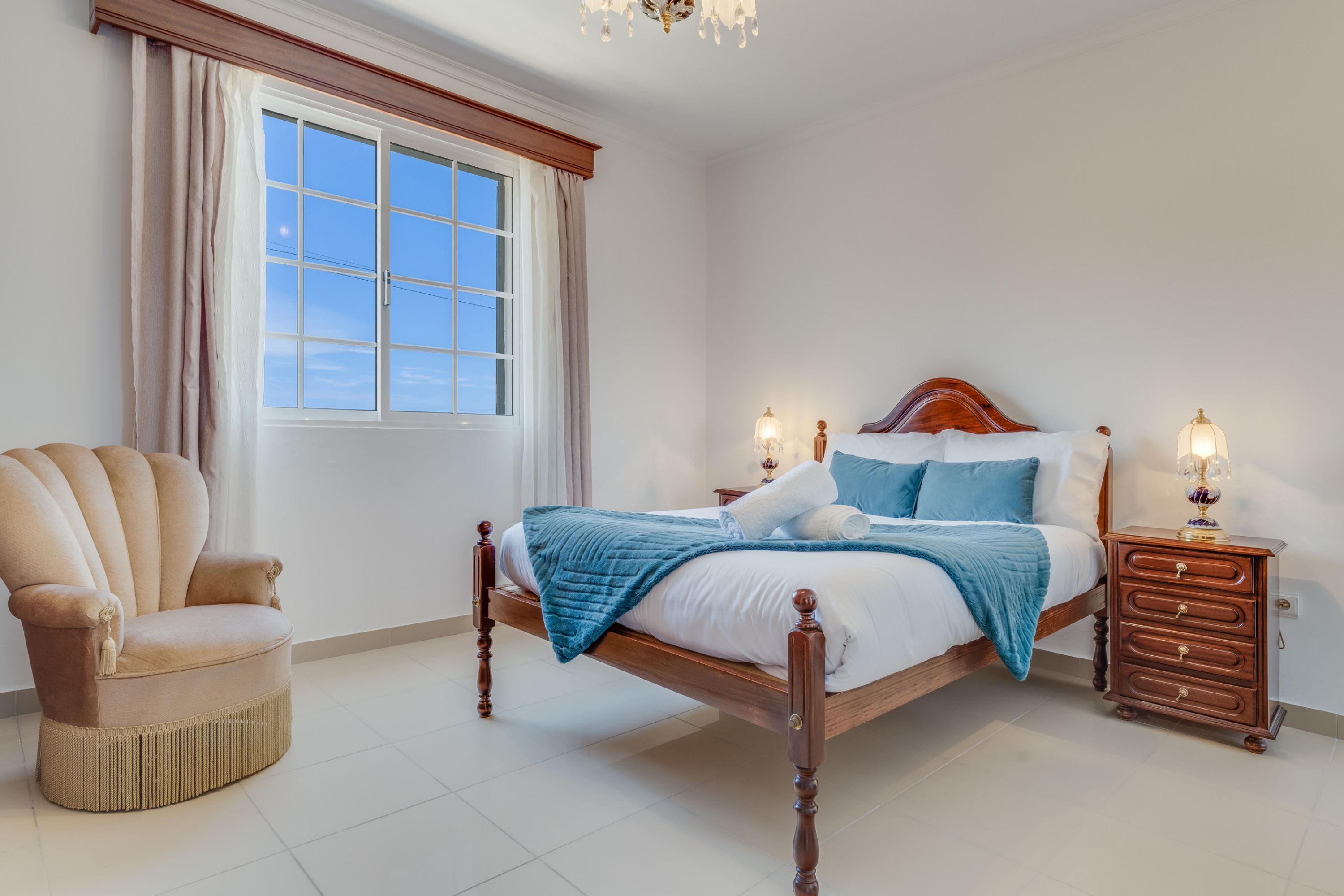 A bedroom with a large bed, a chair, and a nightstand with lamps.