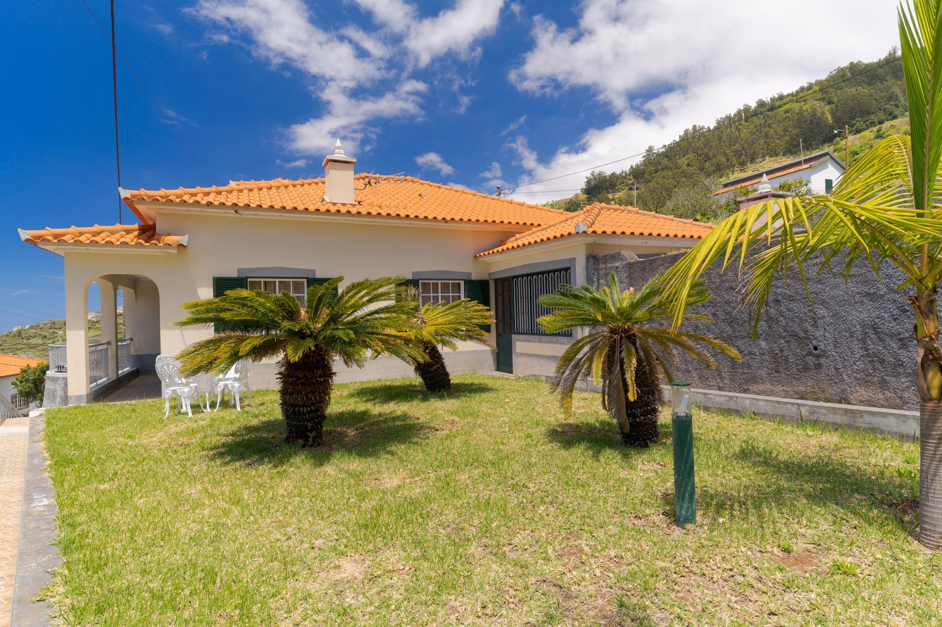 A house with a tiled roof, a covered porch, and a grassy lawn with palm trees.