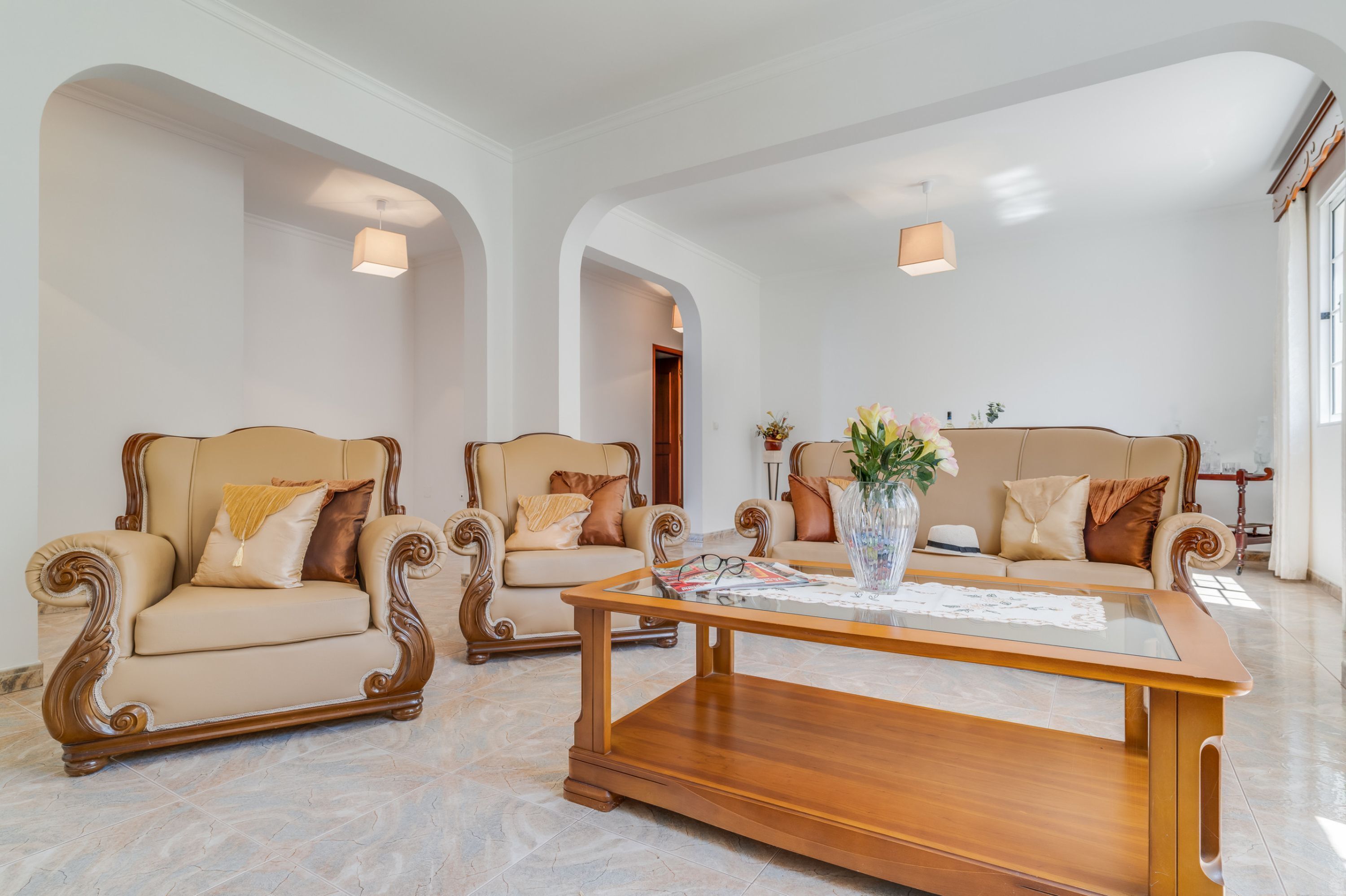 A spacious living room with two beige armchairs and a wooden coffee table, featuring a vase with flowers.