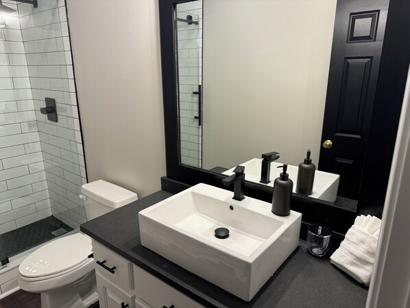 Un baño moderno con lavabo blanco, encimera negra y un espejo grande.