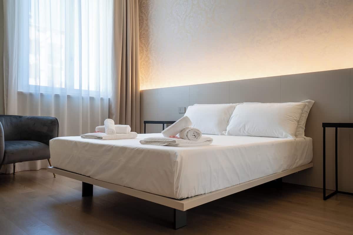 Una habitación de hotel moderna con una cama individual, una silla y un amplio ventanal con cortinas.