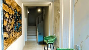 A hallway with a staircase, a green upholstered chair, and a large abstract painting on the wall.