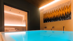 A modern indoor swimming pool with clear blue water, a reception area with a large painting on the wall, and a well-lit room with a patterned wallpaper.