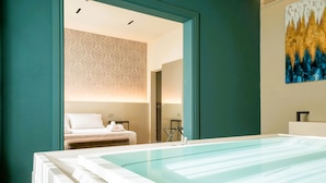 A modern spa room with a glass-enclosed hot tub, a bed with white linens, and a patterned wallpaper.