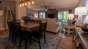 A spacious living room with a wooden dining table, dark chairs, a beige sofa, and a stone fireplace. - Tre L at Watauga Lake - Butler, TN (Johnson County)