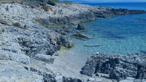 A rocky coastline with clear blue waters and a view of the sea.