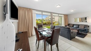 A modern living room with a glass dining table, leather sofa, and a TV mounted on the wall. - 300 Lake Terrace (Taupo)
