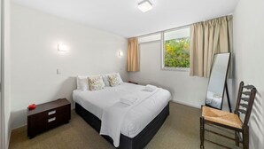 A bedroom with a bed, bedside table, chair, and a large window with curtains. - 300 Lake Terrace (Taupo)
