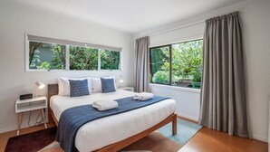 A bedroom with a large bed, a nightstand, a lamp, and a window with curtains.