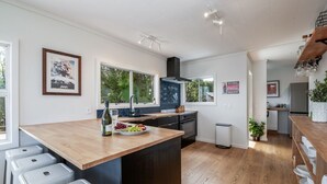 A modern kitchen with a central island, a sink, and a stove. There are bar stools, a trash can, and a potted plant.