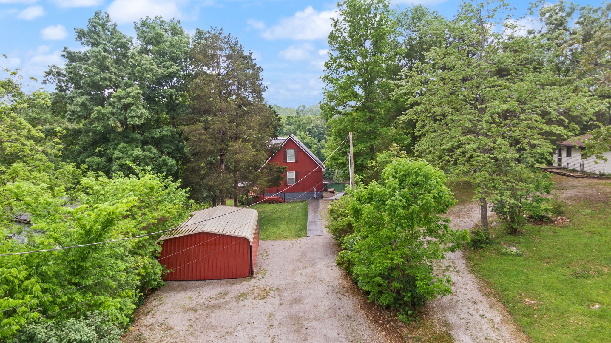 Une grange rouge avec une allée de gravier menant à une maison entourée d’arbres verdoyants et touffus.