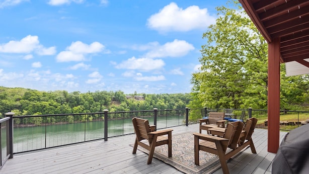 Eine Holzterrasse mit Tisch und Stühlen, mit Blick auf einen See und einen bewaldeten Bereich.