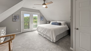 Ein Schlafzimmer mit geneigter Decke, einem Bett mit weißer Bettwäsche, einem Deckenventilator und einer Tür.