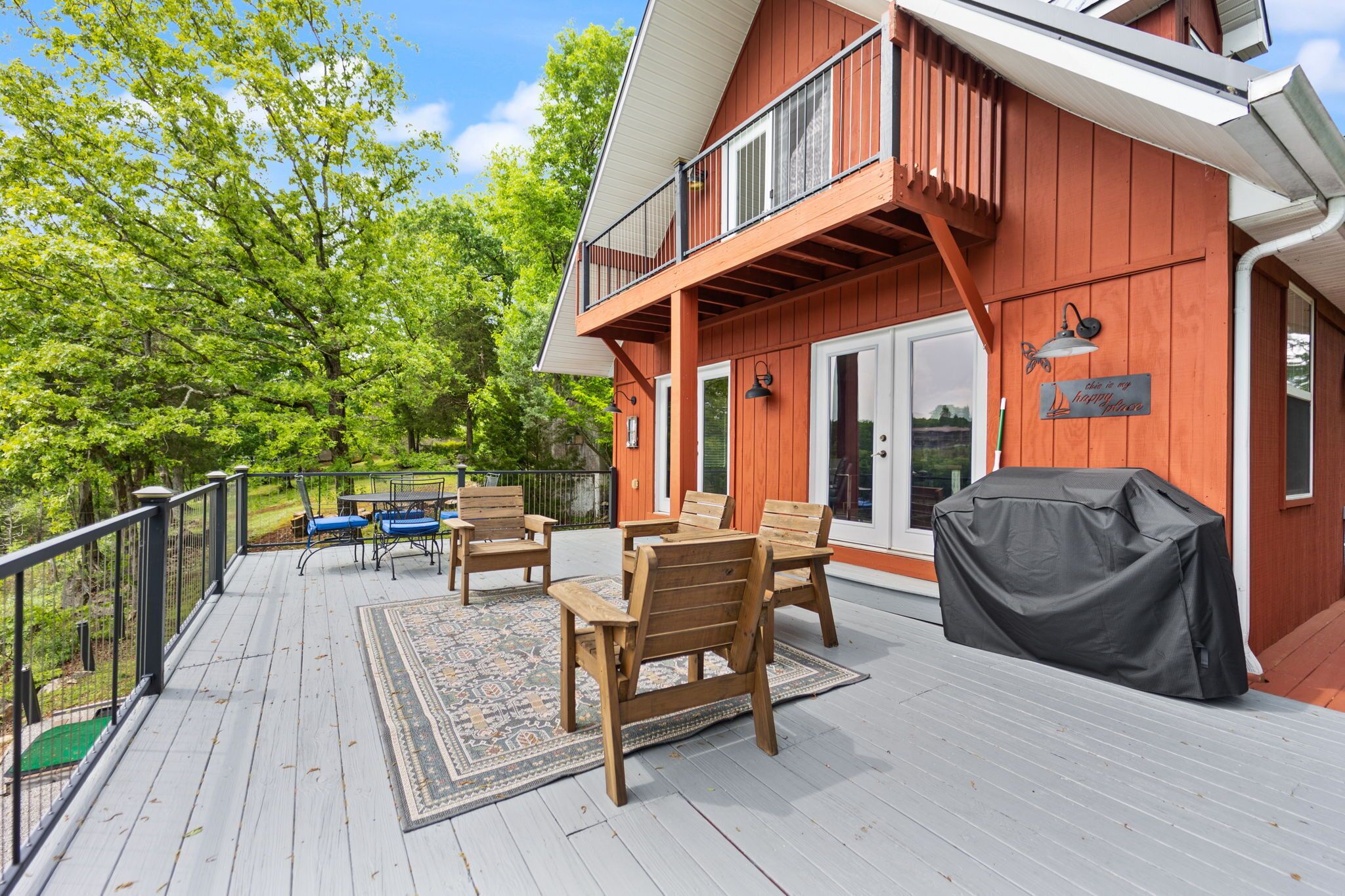 A wooden deck with outdoor furniture, a covered grill, and a view of a forested area.