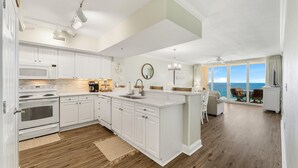 Una cocina moderna con armarios blancos, una isla grande y vistas al océano a través de puertas corredizas de vidrio.