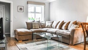 A modern living room with a sectional sofa, a glass coffee table, and a large window with curtains. - 2 bedroom accommodation in Longridge (Longridge)