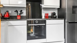A modern kitchen with white cabinets, a Bosch oven, a stainless steel refrigerator, and a red kettle on the countertop. - 2 bedroom accommodation in Longridge (Longridge)