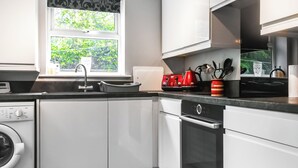 A modern kitchen with white cabinetry, a built-in washing machine, a dishwasher, and a window with a view of greenery. - 2 bedroom accommodation in Longridge (Longridge)