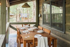 A wooden dining table set with plates and wine glasses, a woven pendant light, and a view of a forest through large windows. - Gym, Sauna, Spa, Firepit, Game Room + Playground! (Fannin County)