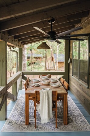 A wooden dining table set with plates and glasses, a ceiling fan, and a view of the outdoors. - Gym, Sauna, Spa, Firepit, Game Room + Playground! (Fannin County)