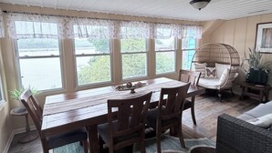 Ein Essbereich mit Holztisch und -stühlen, einem Korbstuhl, einem Teppich und Blick durch große Fenster.