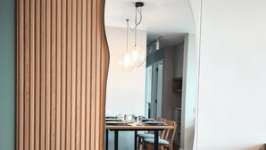 Un interior moderno con un panel de madera, una zona de comedor con mesa y sillas, y un espejo grande que refleja el espacio.