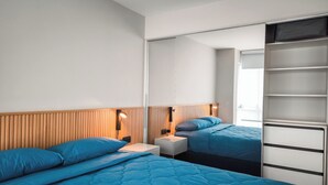 Una habitación de hotel moderna con dos camas, un cabecero de madera, una mesita de noche y un armario.