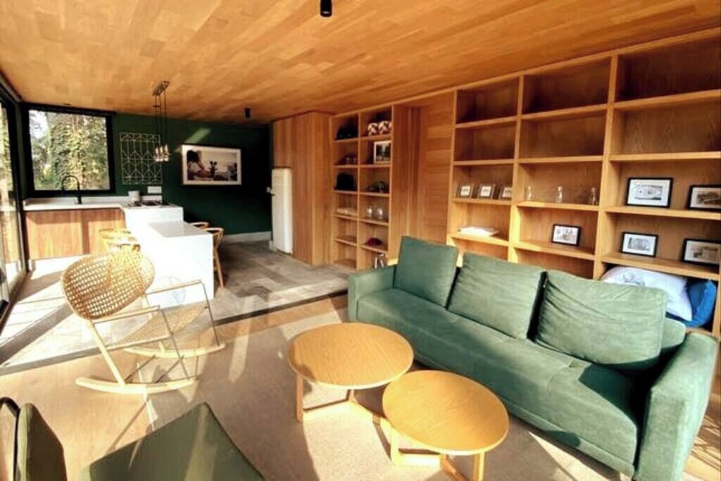 A modern living room with a green sofa, wooden shelves, and a dining area with a white table and chairs.