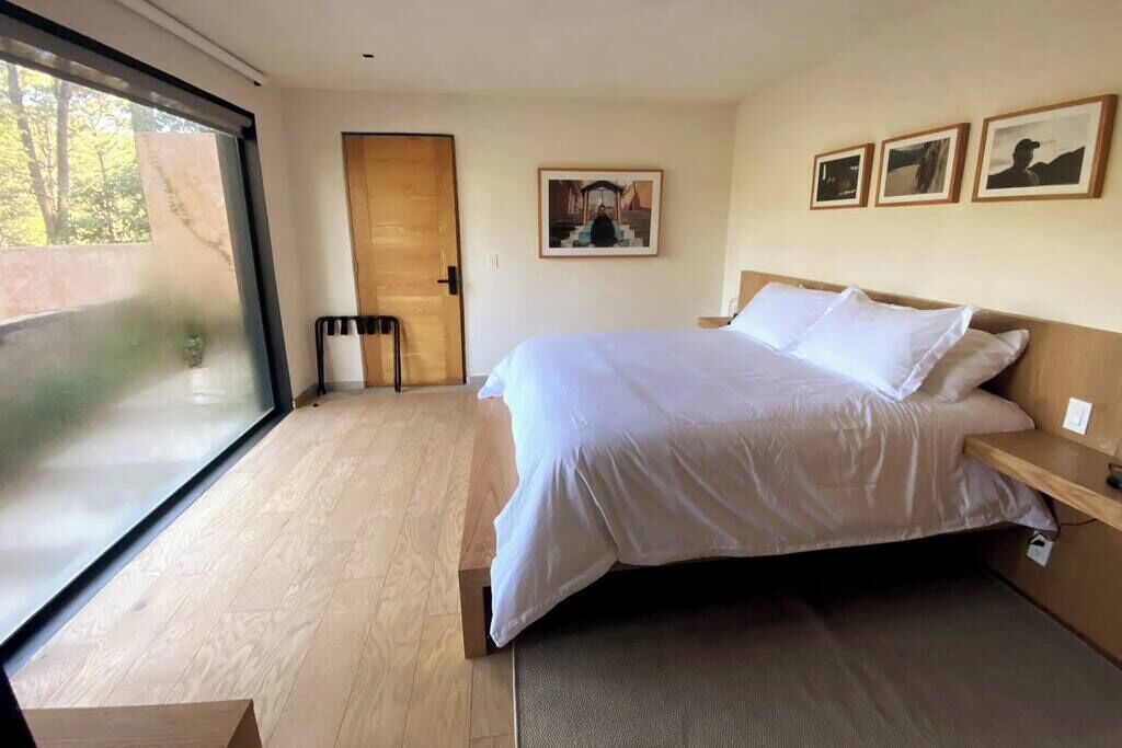 Een moderne slaapkamer met een groot bed, een houten deur en een raam met uitzicht op bomen.
