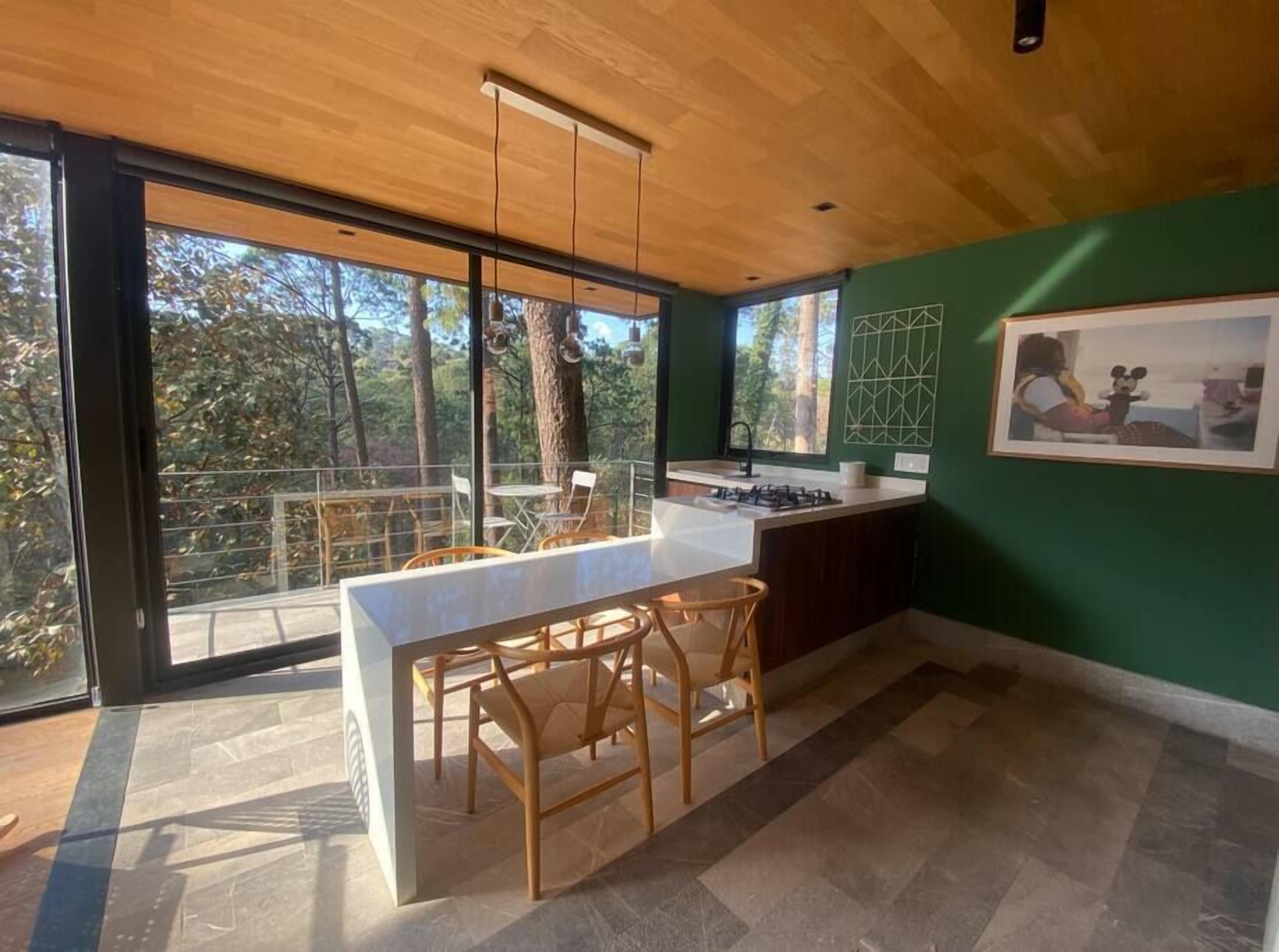 Una cucina moderna con una grande isola, sedie di legno e vista sugli alberi attraverso ampie finestre.
