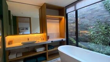 A modern bathroom with a freestanding bathtub, wooden shelving with towels, and a large window with a stone wall view.