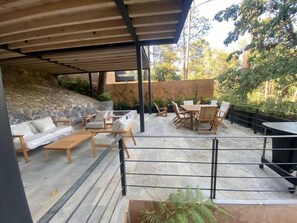 A covered outdoor patio with stone flooring, wooden furniture, and a stone wall backdrop.
