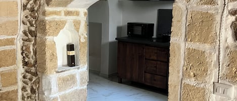 Un arc en pierre mène à une cuisine équipée d’un four à micro-ondes et de meubles de rangement en bois.