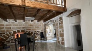 Una habitación amplia con una pared de piedra, una chimenea y un comedor con sillas.