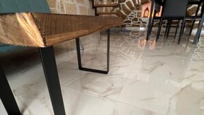 Un área de comedor con un banco de madera y patas de metal negro, una pared de piedra y un suelo de baldosas.