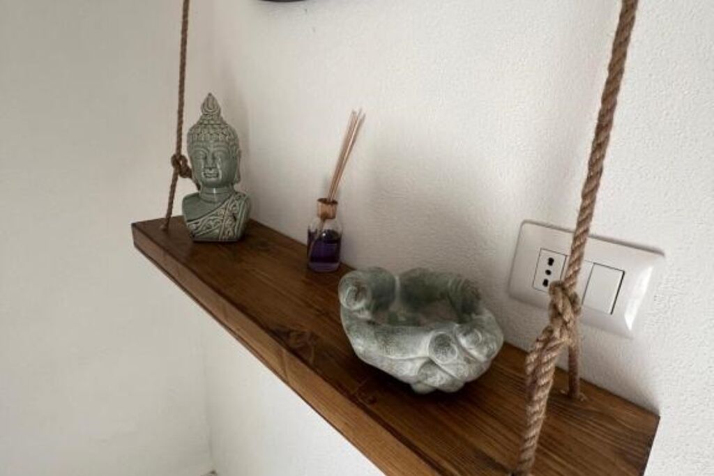 Estante de madeira com uma estátua de Buda, um pequeno vaso com raminhos e uma escultura de pedra.