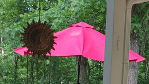 Una terraza de madera con una mesa, sillas, un adorno solar colgante y un paraguas rojo.