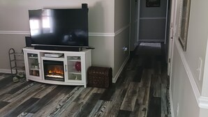 Una sala de estar con una televisión de pantalla plana sobre un mueble blanco, una chimenea y piso de madera.