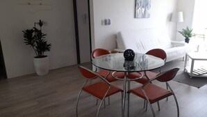 A modern dining area with a glass table and red chairs, a white sofa, and a potted plant. - Departamento en Tequesquitengo (Tequesquitengo)