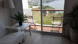 A balcony with a view of a lake and town, a white sofa, a small table with a plant, and a potted plant beside the sofa. - Departamento en Tequesquitengo (Tequesquitengo)