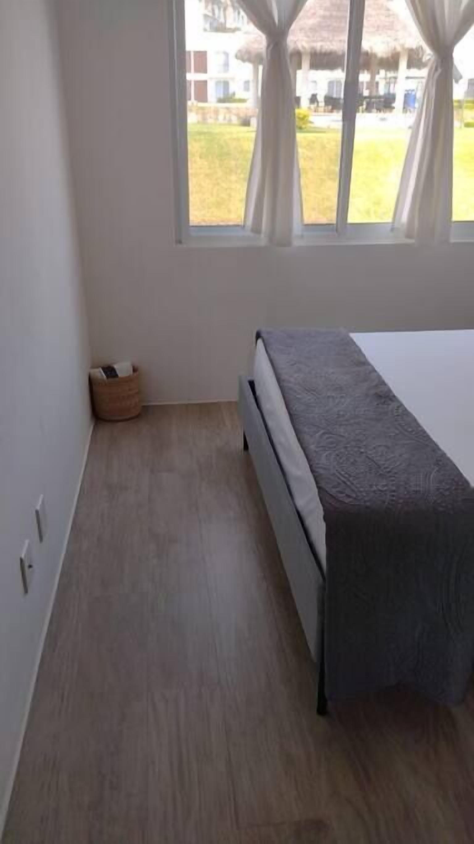 Une chambre à coucher avec un lit, une fenêtre avec des rideaux, un plancher en bois et un petit panier.