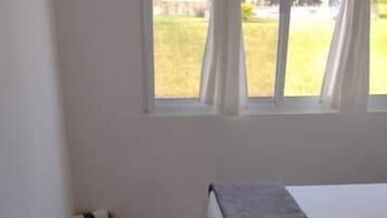 Une chambre à coucher avec un lit, une fenêtre avec des rideaux, un plancher en bois et un petit panier.